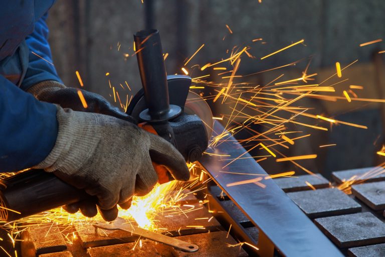 As a master metal worker grinds metal on a grinder there is a spark in the factory as he works in